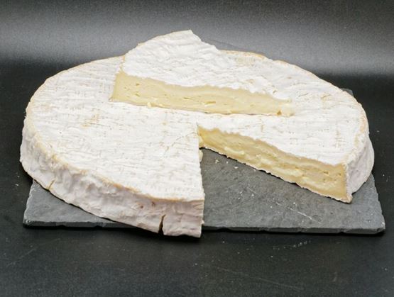Wheel of Brie de Meaux with a wedge cut out, on a black slate.