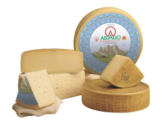 Whole and cut Asiago cheeses on a yellow wrapper.
