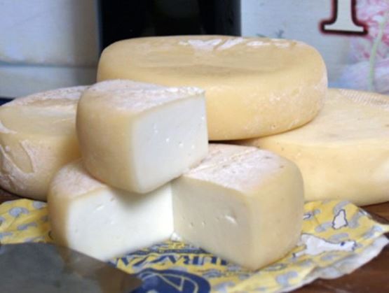 Murazzano cheese with white paste and thin rind, displayed on a wooden board.
