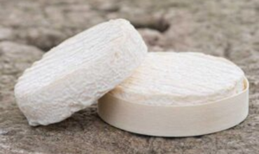 Image montrant deux fromages Le Pérail à croûte fine et fleurie, posés sur une surface en pierre. L’un est présenté dans une boîte en bois clair, l’autre est posé à côté, laissant apparaître sa texture crémeuse et sa forme ronde typique.