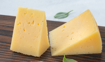 deux morceau de fromage posé sur une planche en bois foncé sur laquelle se trouvent deux feuilles vertes