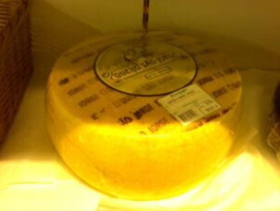 Fromage entier São Jorge DOP sous film plastique, avec étiquette circulaire noire sur le dessus et inscriptions répétées sur la croûte jaune.