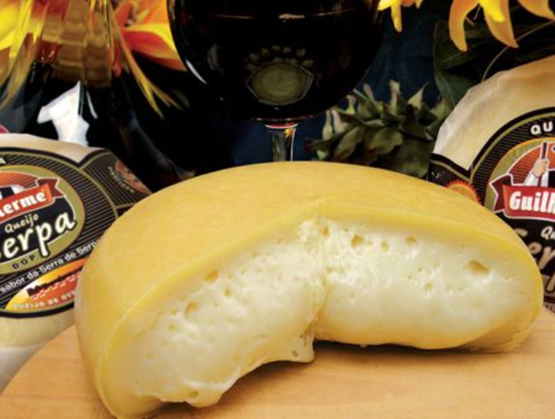 Fromage portugais Serpa DOP entamé, à pâte molle et croûte jaune, présenté sur une planche en bois avec un verre de vin rouge en arrière-plan.
