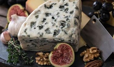 Morceau de fromage sur une planche, entouré de figues et de noix