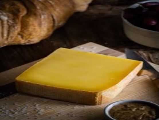 Morceau de Tiroler Bergkaese sur une planche en bois avec des cristaux de sel et un petit pot contenant une crème ou une sauce 
