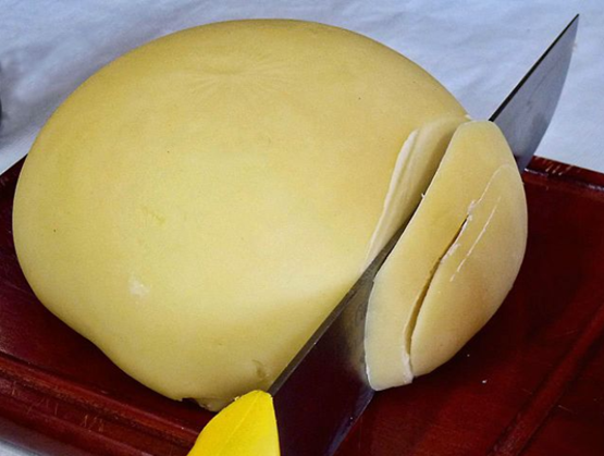 morceau de tetilla aop posé sur une planche en bois à découpée. le morceau est coupé par un couteau